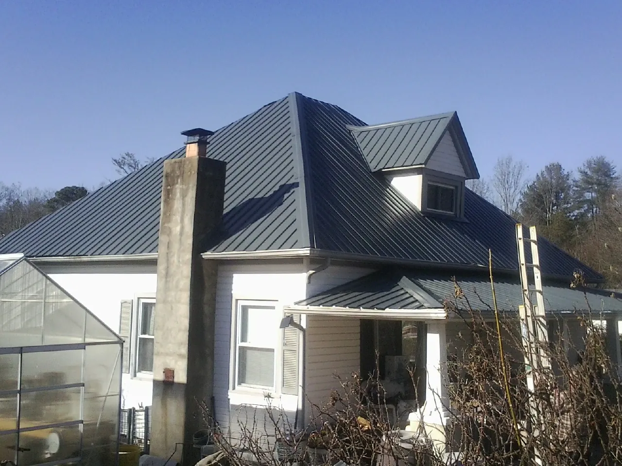 Dark blue standing seam metal roof on a white farmhouse with dormer — Slate & Tile Roof Repair by Roofing Brothers in Dougherty