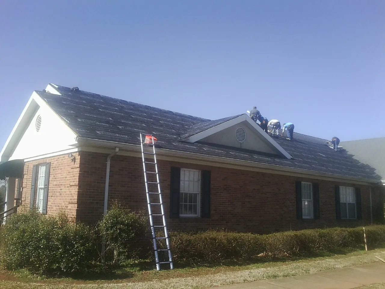 Crew tearing shingles off a brick ranch roof with a ladder set — Metal Roof Repair work by our crew in Dougherty