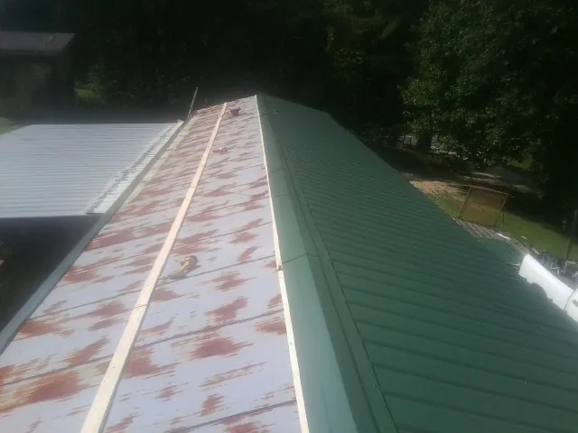 Old rusted panels beside newly installed green metal roofing — Wind Damage Roof Repair by Roofing Brothers in Dougherty