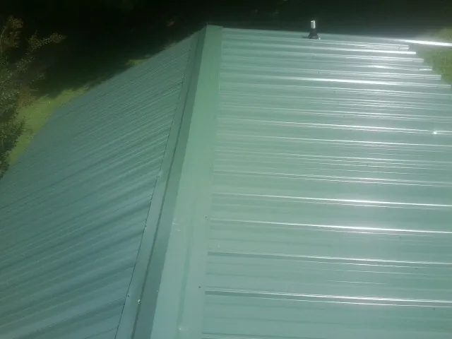 New green metal panels meeting at the ridge of a roof — Flat Roof Repair work by our crew in Dougherty