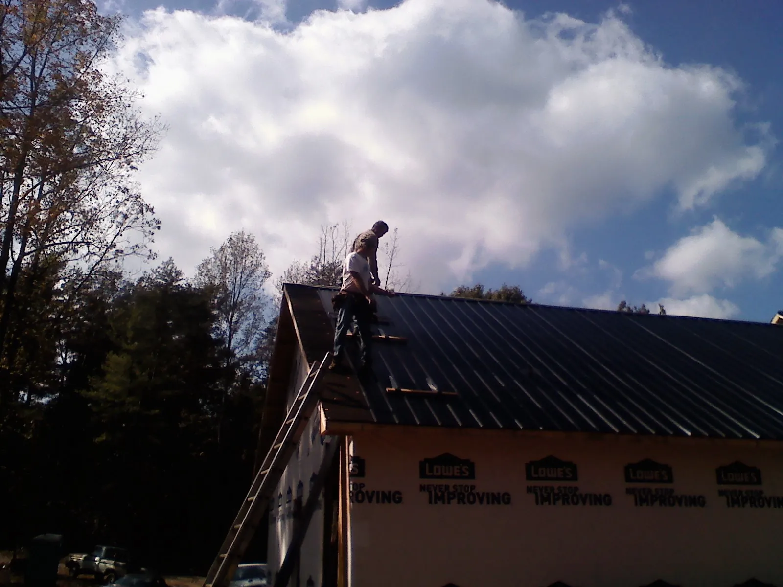 Roofer fastening dark metal panels high against a cloudy sky, from a Roof Inspection job in Dougherty