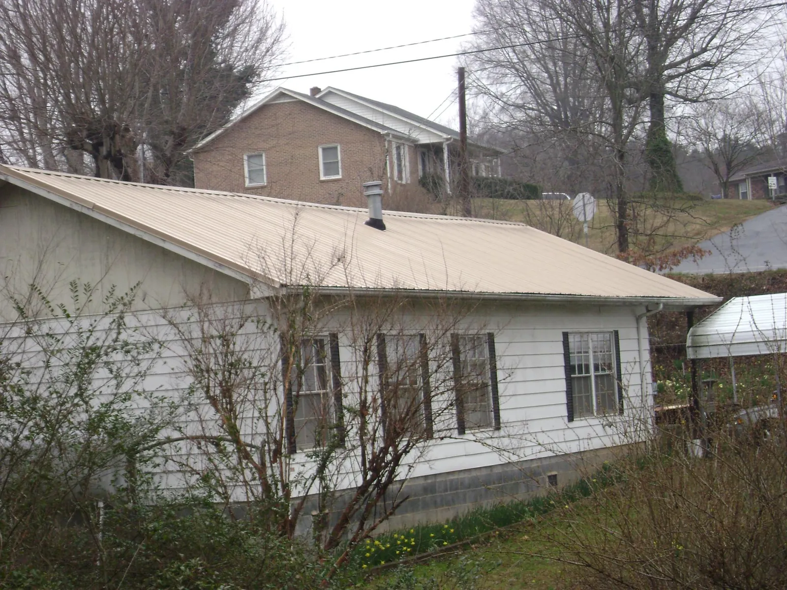 Tan metal roof on a white sided house set into a hillside — Commercial Roofing by Roofing Brothers in Dougherty